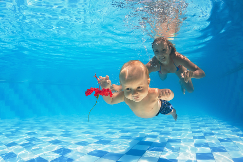 In the pool young mother teaches to swim 10 month old baby - dive with cheerful boy deep into the water for a beautiful red flower healthy lifestyle and children swimming lessons with an instructor